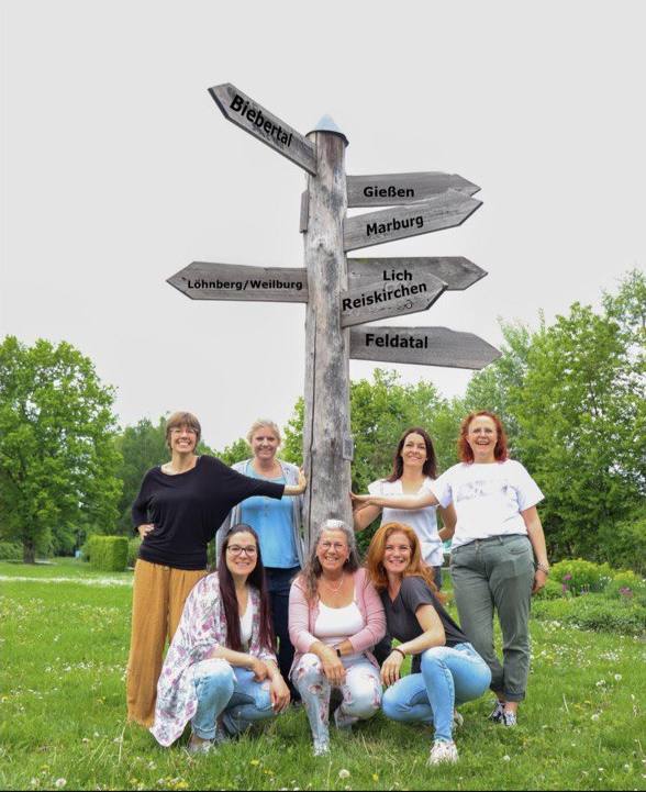 Das Bild zeigt verschiedene Mitglieder des Mütterpflege Netzwerks Mittelhessen und auf einem Schild die verschiedenen Orte, in denen sie arbeiten.